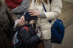 A close up of a young girl leaning against her mother, who places her hands on her back and head.