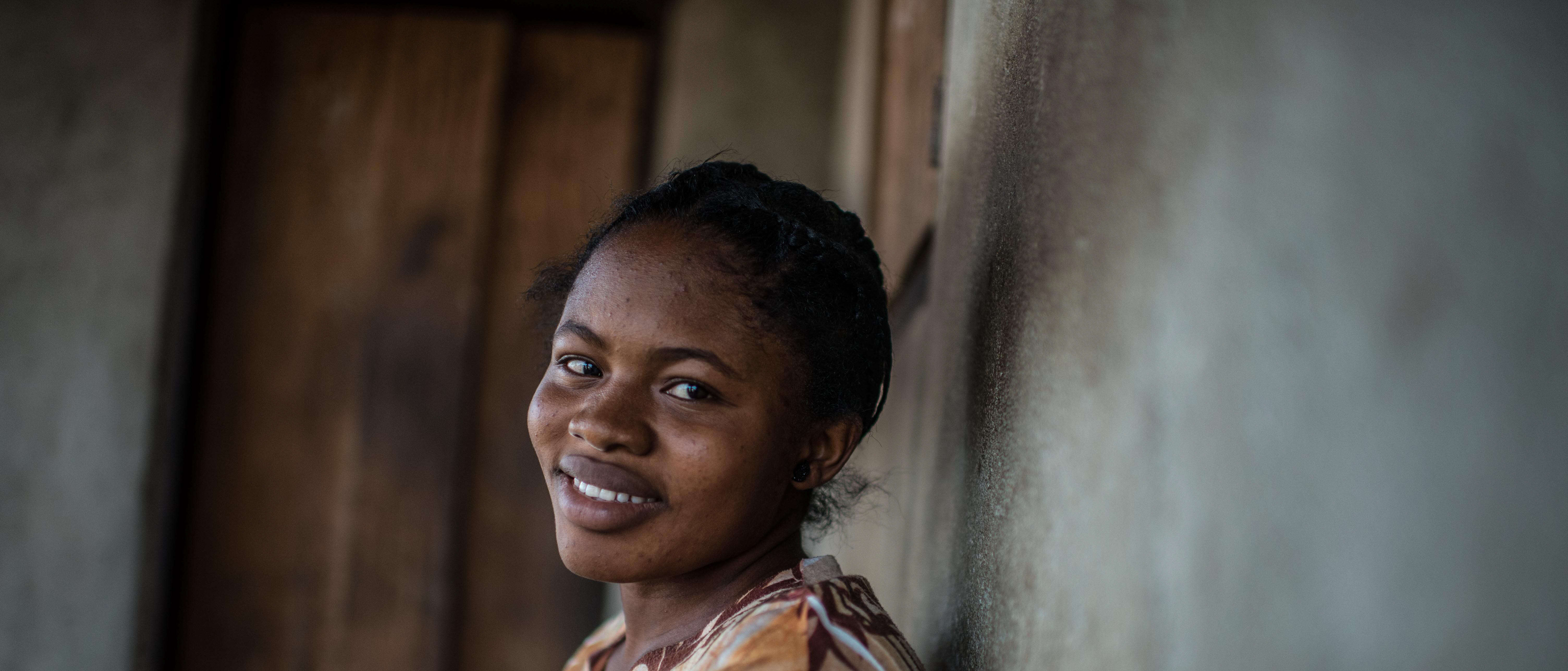 A woman stands against a wall and smiles.