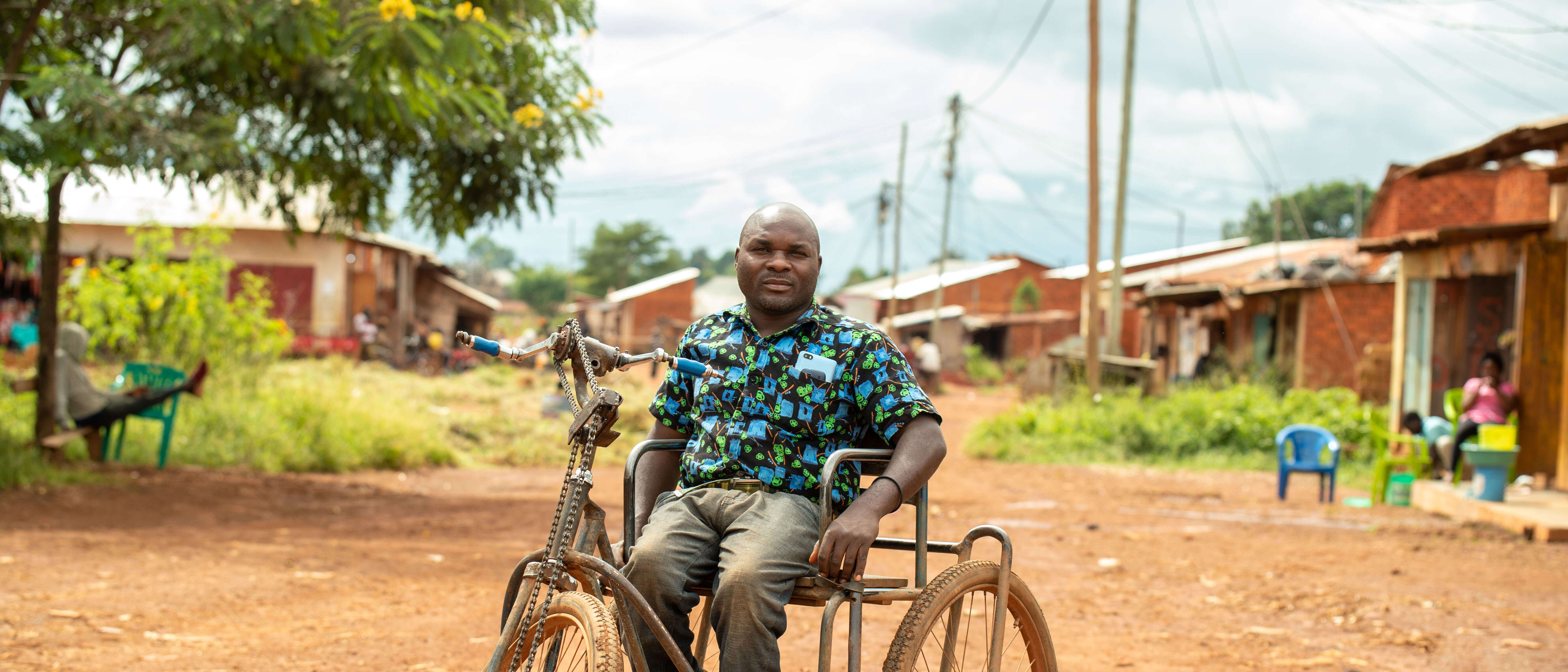 A man poses for a photo while sitting in a wheelchair and hand-cranked bicycle.