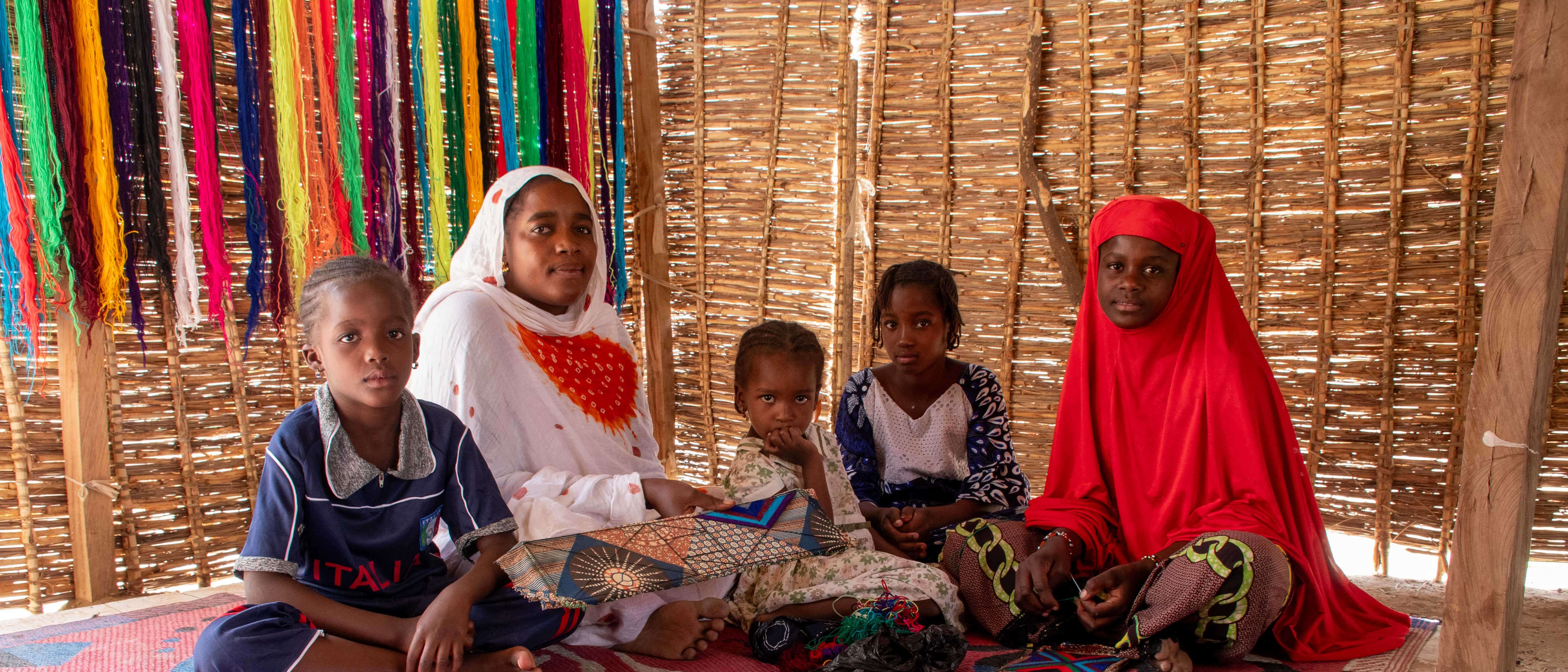 A caregiver sits on the floor of a makeshift shelter with four children.