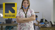 Dr. Edna Patricia Gomez stands in scrubs with her arms crossed. She has mask at her chin and there is an IRC logo behind her.